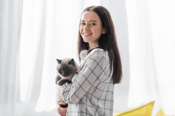 Feliz jovem mulher olhando para a câmera enquanto de pé com gato em casa — Fotografia de Stock