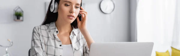 Young freelance touching wireless headphones while working at home, banner — Stock Photo