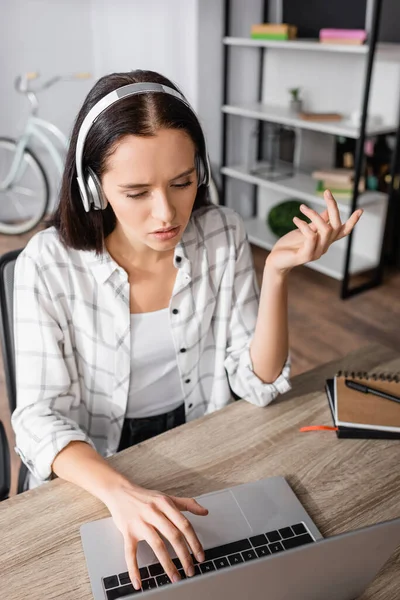 Freelancer desencorajado em fones de ouvido digitando no laptop em casa — Fotografia de Stock