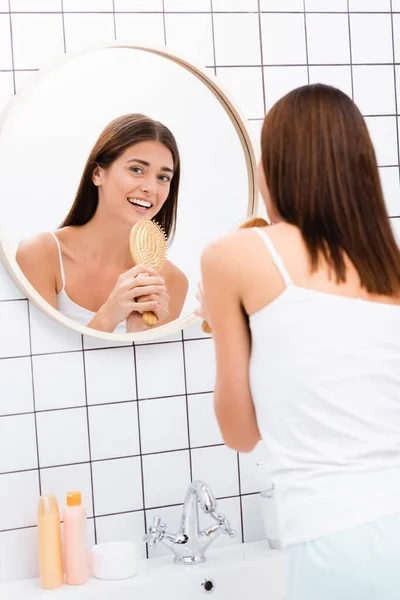 Felice giovane donna che canta con spazzola vicino specchio in bagno — Foto stock