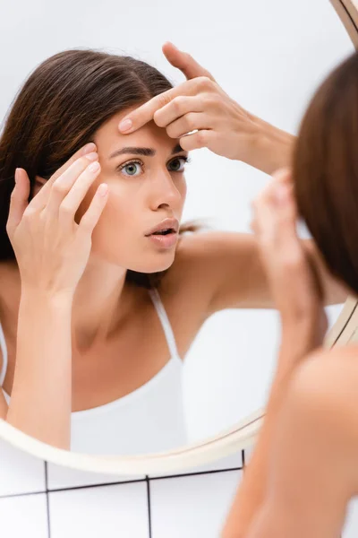 Displeased young woman touching face while looking in mirror, blurred foreground — Stock Photo