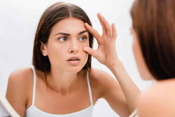 Worried young woman looking in mirror and touching face, blurred foreground — Stock Photo