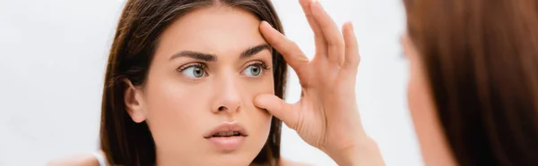 Junge Frau berührt Gesicht beim Blick in den Spiegel, verschwommener Vordergrund, Banner — Stockfoto