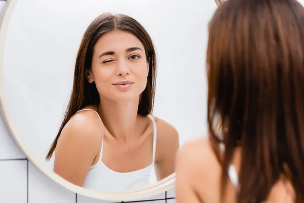Young cheerful woman winking near mirror in bathroom, blurred foreground — Stock Photo