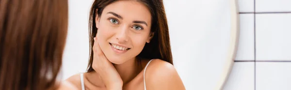 Femme heureuse touchant le visage près du miroir dans la salle de bain, avant-plan flou, bannière — Photo de stock