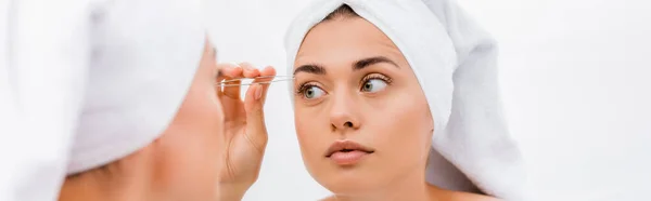 Femme avec serviette blanche sur la tête pinçant les sourcils près du miroir, avant-plan flou, bannière — Photo de stock