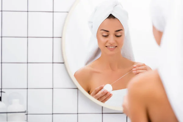 Mujer joven con toalla blanca en la cabeza sosteniendo hilo dental cerca del espejo en el baño, borrosa primer plano - foto de stock