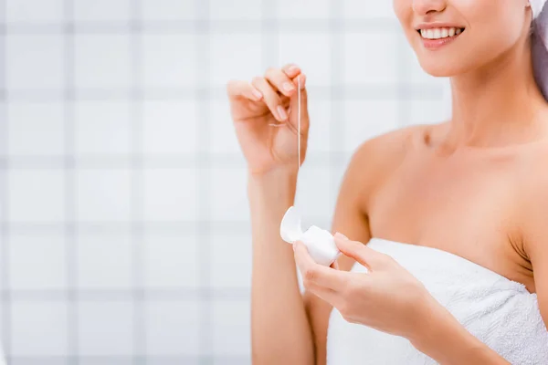 Частичный вид улыбающейся женщины, держащей зубную нить в ванной комнате — стоковое фото