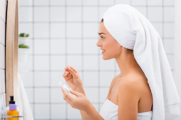 Vista lateral de la mujer con toalla blanca en la cabeza sosteniendo hilo dental en el baño - foto de stock