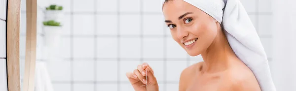 Mujer alegre con toalla de rizo blanco en la cabeza mirando a la cámara mientras sostiene el hilo dental, pancarta - foto de stock