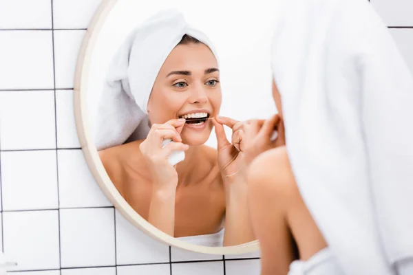 Femme avec serviette éponge blanche sur les dents de nettoyage de la tête avec fil dentaire dans la salle de bain, avant-plan flou — Photo de stock
