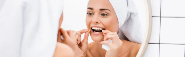 Mujer con toalla en la cabeza dientes de hilo dental cerca del espejo en el baño, primer plano borrosa, pancarta - foto de stock