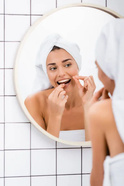 Giovane donna con asciugamano bianco sulla testa denti filo interdentale vicino specchio in bagno, primo piano sfocato — Foto stock