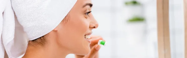 Vista laterale della donna con asciugamano bianco sulla testa che tiene lo spazzolino in bagno, banner — Foto stock