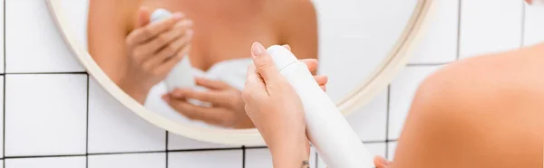 Visión parcial de la mujer que sostiene desodorante cerca de reflejo borroso en el espejo, pancarta - foto de stock