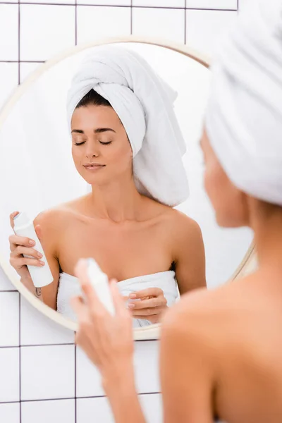 Молодая женщина с белым полотенцем на голове наслаждается ароматом дезодоранта в ванной комнате, размытый передний план — стоковое фото