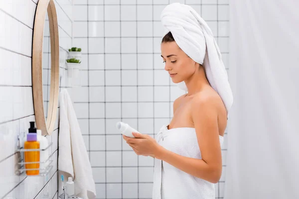 Young woman with white towel on head holding deodorant in bathroom — Stock Photo