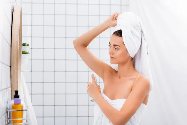 Jeune femme, enveloppée dans des serviettes éponge, application de déodorant dans la salle de bain — Photo de stock