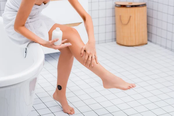 Частичный вид женщины, наносящей лосьон для тела на ногу, сидя на ванне — стоковое фото