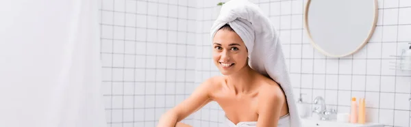 Щаслива молода жінка з білим рушником на голові посміхається на камеру у ванній кімнаті, банер — стокове фото