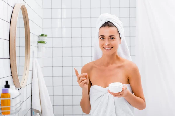 Femme gaie avec crème visage sur le nez souriant à la caméra dans la salle de bain — Photo de stock