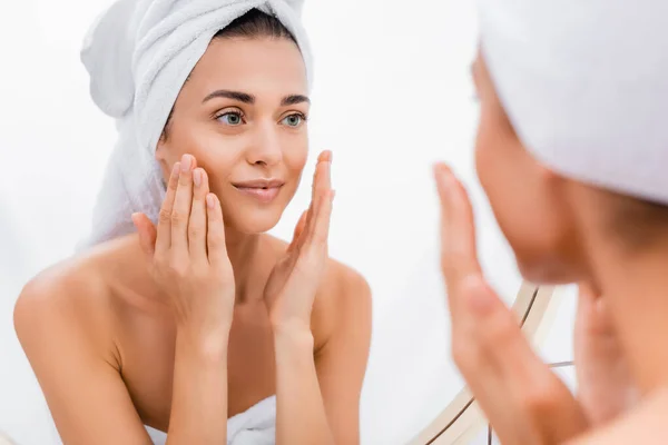 Giovane donna con asciugamano sulla testa applicare scrub viso mentre si guarda allo specchio, primo piano sfocato — Foto stock