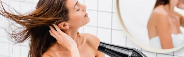 Young woman drying hair with closed eyes near blurred reflection in mirror, banner — Stock Photo