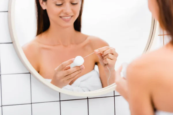 Selective focus of dental floss in hands of young woman near mirror in bathroom, blurred foreground — Stock Photo