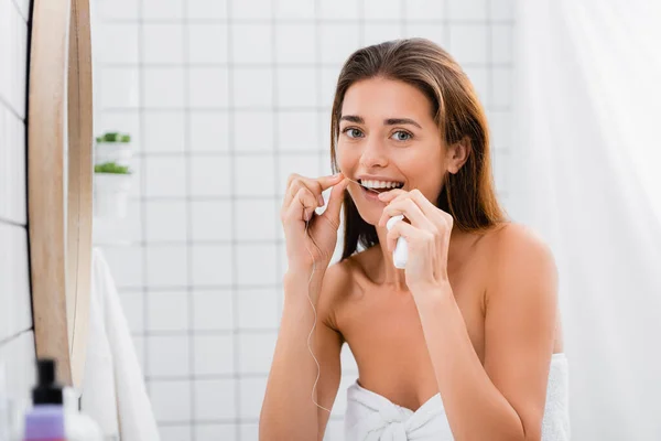 Mujer joven mirando a la cámara mientras limpia los dientes con hilo dental en el baño - foto de stock