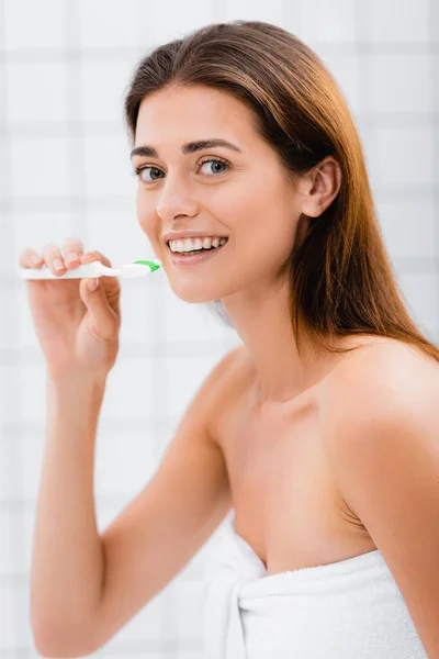 Mulher feliz sorrindo para a câmera enquanto segurando escova de dentes no banheiro — Fotografia de Stock