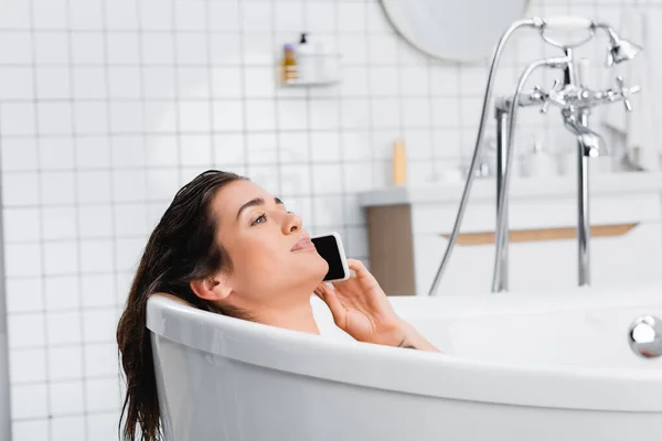 Jeune femme souriante qui prend son bain et parle sur son téléphone portable — Photo de stock