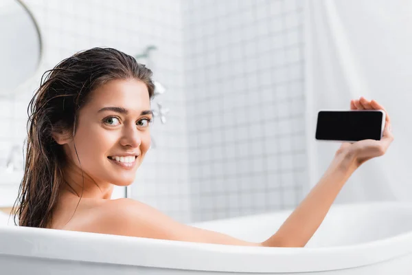 Счастливая молодая женщина, делающая селфи во время купания и улыбающаяся на камеру — стоковое фото