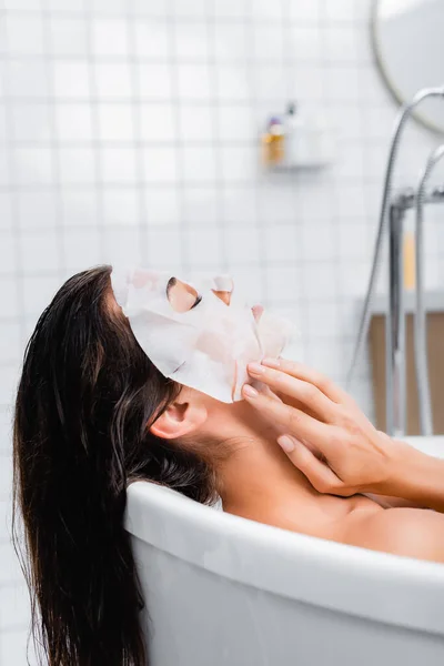 Jeune femme touchant masque facial tout en prenant un bain à la maison — Photo de stock