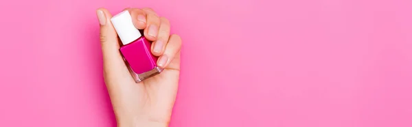 Vista dall'alto della mano femminile curata con bottiglia di smalto lucido su sfondo rosa, banner — Foto stock