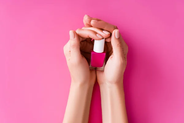 Partial view of groomed female hands with bottle of nail varnish on pink background — Stock Photo