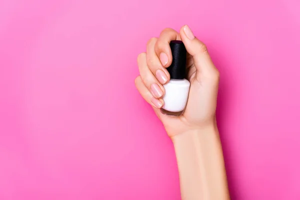 Partial view of woman holding bottle of white nail enamel on pink background — Stock Photo