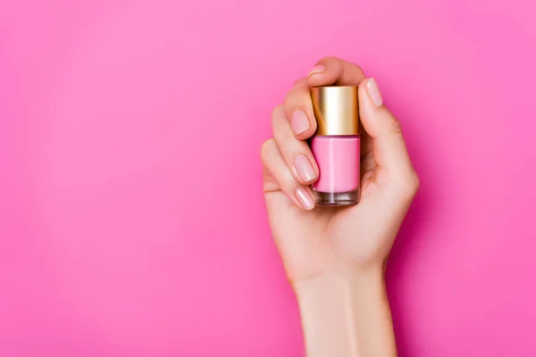 Vue du dessus de la main féminine toilettée avec flacon de vernis pastel sur fond rose — Photo de stock