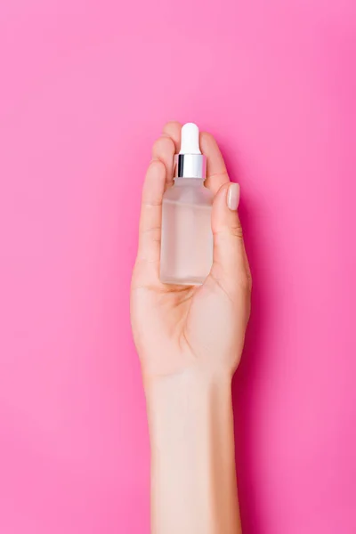 Vista dall'alto della mano femminile curata con bottiglia di dispositivo di rimozione cuticole su sfondo rosa — Foto stock