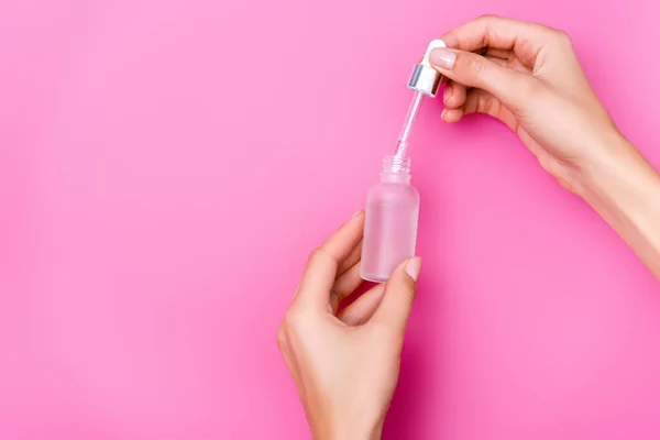 Partial view of woman holding dropper and bottle of cuticle remover on pink background — Stock Photo