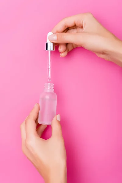 Teilansicht einer Frau mit Tropfer und Flasche Nagelhautentferner auf rosa Hintergrund — Stockfoto