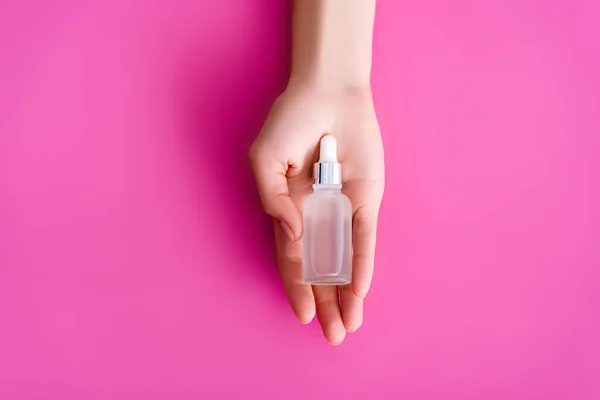Vista dall'alto della mano femminile curata con flaconcino di dispositivo di rimozione cuticole su sfondo rosa — Foto stock