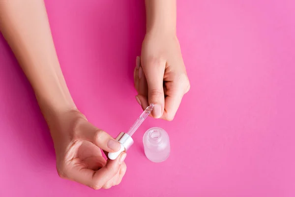 Cropped view of woman applying cuticle remover with dropper on pink background — Stock Photo