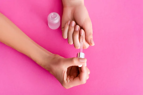 Partial view of woman applying cuticle remover with dropper on pink background — Stock Photo