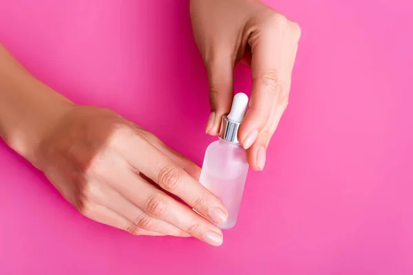 Cropped view of woman holding vial with cuticle remover on pink background — Stock Photo