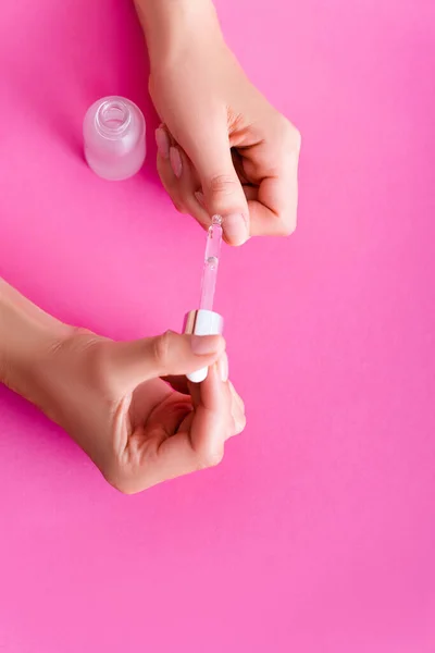 Vue partielle de la femme appliquant décapant cuticule avec compte-gouttes sur fond rose — Photo de stock