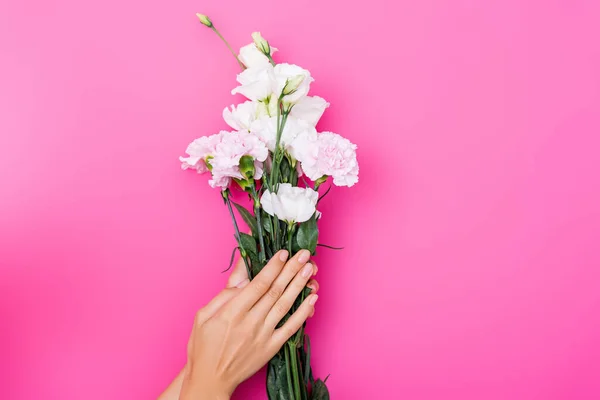Partial view of woman with shiny manicure holding eustoma and carnation flowers on pink background — Stock Photo