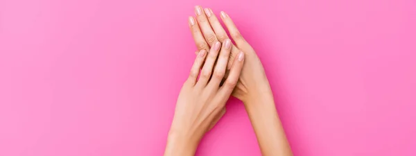 Vista superior de mãos femininas com unhas cobertas com verniz de unha pastel no fundo rosa, banner — Fotografia de Stock