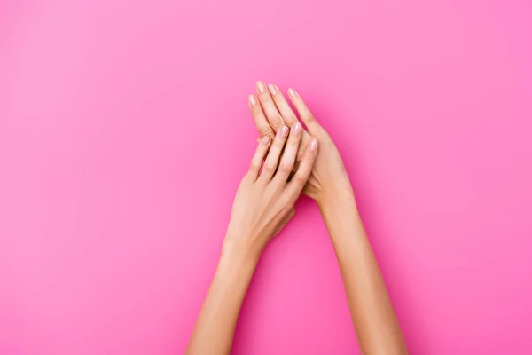 Vue de dessus des mains féminines toilettées avec des ongles brillants sur fond rose — Photo de stock