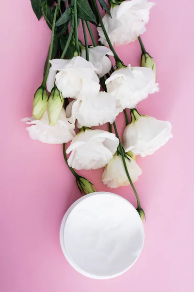 Vista superior de crema cosmética y flores de eustoma blanco sobre fondo rosa - foto de stock