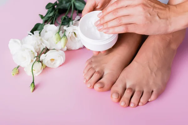 Partial view of woman with cosmetic cream near white eustoma flowers on pink background — Stock Photo